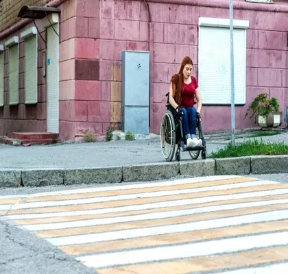 Una chica joven en silla de ruedas dispuesta a pasar por un paso de peatones, pero no puede debido al bordillo que impide seguir su camino
