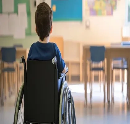 Un niño, de espaldas, sentado en una silla de ruedas, dentro de un aula escolar