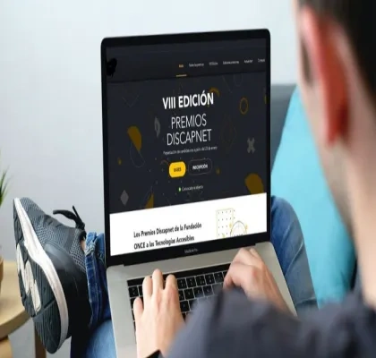 hombre sosteniendo un ordenador portátil con la pantalla encendida en la web oficial de los Premios Discapnet