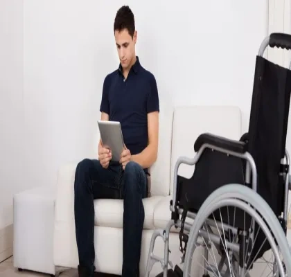 Persona con movilidad reducida sentado en el sillón junto a su silla de ruedas, mientras usa la tablet