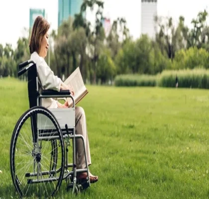 Una mujer con discapacidad en silla de ruedas, leyendo en un parque