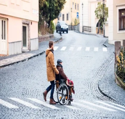 Una persona joven paseando a una persona mayor en silla de ruedas