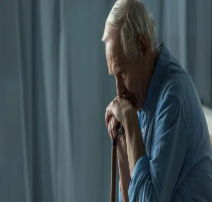 Persona mayor sentada en el sofa con la barbilla encima de su bastón