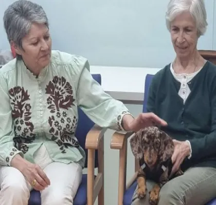 Dos personas mayores junto a un perro en una sesión de terapia asistida con animales (Fuente: Neurovida)