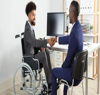 Dos trabajadores, uno de ellos en silla de ruedas y otro sin discapacidad visible, chocando sus manos en forma de acuerdo alcanzado en un despacho de la oficina