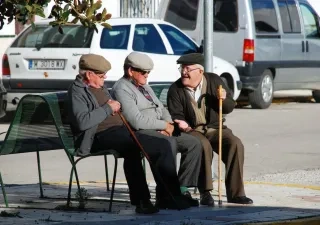 Tres mayores conversan sentados en un banco 