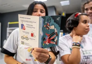 Participantes en una actividad del proyecto Camino + Accesible sostienen un folleto informativo de El Camino con Correos, que recoge servicios para peregrinos como el transporte de equipajes, el envío de bicicletas y la consigna en Santiago de Compostela.