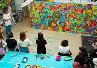 Foto Creación Ilusión con varias personas presenciando la obra, que es un mural grande con mucho colorido.