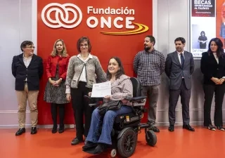 una alumna en silla de ruedas con un certificado en la mano, detras ptras personas con el logo de fundación once