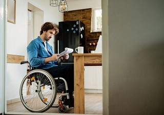 Una persona en silla de ruedas leyendo un documento en su casa (Fuente: Servimedia)