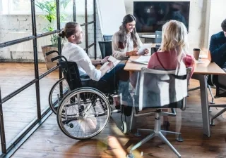 Cuatro personas trabajando en una oficina, manteniendo una reunión. Una de ellas va en silla de ruedas, ejemplarizando la inclusión laboral