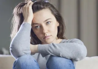 Una mujer sentada en el sofá de rodillas tocándose el pelo