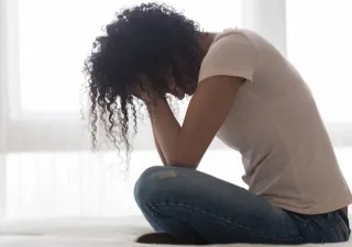 Mujer en la cama sentada con los brazos en la cara mostrando soledad o tristeza