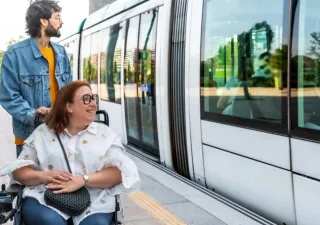 Un hombre sin discapacidad junto a una mujer en silla de ruedas esperando en el andén al tren