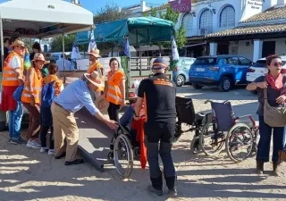 Varias personas voluntarias subiendo a una usuaria en silla de ruedas a un autobús turístico.