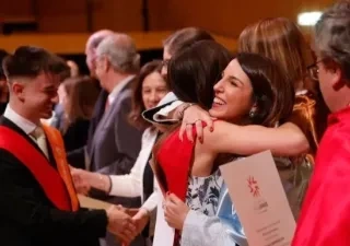 Una foto de dos alumnos recibiendo el título de los profesores de la universidad y dándose un abrazo