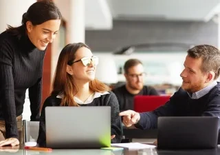 Tres personas hablando delante de la pantalla de un ordenador en la oficina