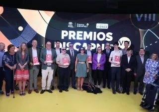 Foto de grupo de las personas premiadas, representantes institucionales y asistentes durante la VIII edición de los Premios Discapnet de Fundación ONCE. Los participantes posan sobre un escenario frente a una gran pantalla con el texto “Premios Discapnet VIII” y los logotipos de Fundación ONCE y Grupo Social ONCE. Varias personas sostienen los galardones, mientras que en la primera fila también aparecen una persona usuaria de silla de ruedas eléctrica y un perro guía tumbado en el suelo