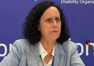 Ana Peláez delante de un micrófono en una sala de prensa, con un fondo azul de logos a su espalda