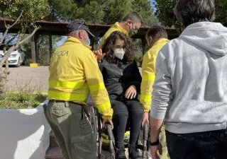 Tres técnicos de emergencias levantando a pulso a una usuaria en silla de ruedas, haciendo un ejemplo práctico con un supervisor que explica