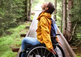 Una mujer en silla de ruedas posando en un camino de madera rodeado de árboles