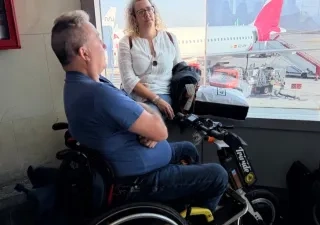 Persona con silla de ruedas esperando a embarcar en un avión, que puede verse al fondo por una cristalera