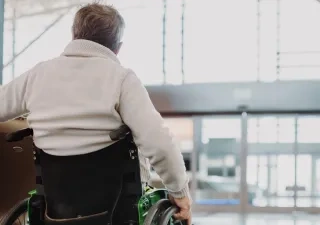 Un hombre con silla de ruedas, al que se ve de espaldas, movíendose por el aeropuerto con su maleta