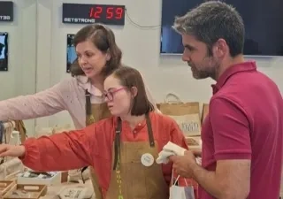 Dos profesores atendiendo a una alumna del CEE ACHIRA, enseñándola a vender en el mercadillo