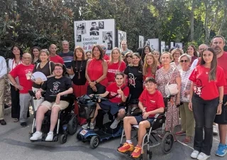 Grupo de personas reunidas al aire libre en un parque junto a varios paneles expositivos de la campaña "Escuchar cambia la historia". Algunas personas utilizan sillas de ruedas manuales y motorizadas. La imagen muestra a participantes, familiares y personas colaboradoras posando frente a la exposición fotográfica dedicada a visibilizar la realidad de quienes conviven con la distrofia muscular de Duchenne.