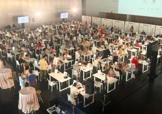 Salón de juntas con varias mesas y muchos ponentes y oyentes