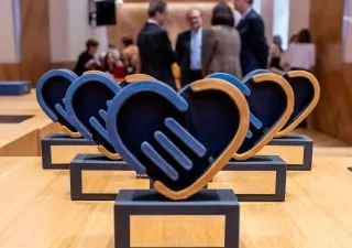 Los 5 premios que se entregarán en la gala delante y, al fondo, personas organizadoras