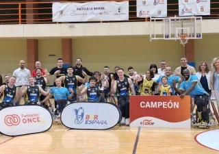 Equipo y cuerpo técnico del CD Ilunion posan en una pista cubierta de baloncesto tras proclamarse campeones de la Supercopa de España de baloncesto en silla de ruedas. En el centro de la imagen, varios jugadores en silla de ruedas sostienen un trofeo y realizan un gesto con cuatro dedos levantados. En la parte frontal aparecen paneles con los logotipos de Fundación ONCE, BSR España y un cartel con la palabra “CAMPEÓN”. Al fondo se observan canastas y pancartas institucionales de Castilla-La Mancha y BSR Esp