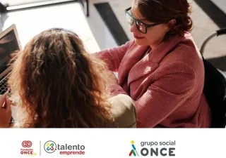 Dos mujeres, una con discapacidad, mirando a la pantalla del ordenador mientras trabajan