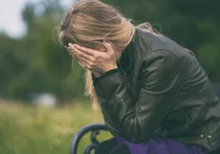 Mujer jóven sentada en un banco se tapa la cara con las manos