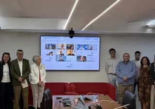 Participantes del grupo de la reunión con una pantalla digital en la que estaban proyectando una sesión virtual con otros participantes