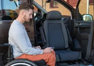 Una persona en silla de ruedas junto a un vehículo adaptado con asiento giratorio para ir de copiloto (Fuente: Rehatrans)