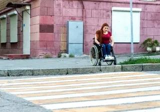 Una chica joven en silla de ruedas dispuesta a pasar por un paso de peatones, pero no puede debido al bordillo que impide seguir su camino