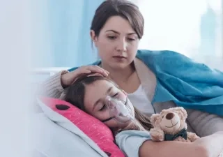 Madre cuidando a su hija con fibrosis quística que está en la cama usando un tratamiento respiratorio