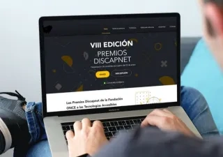 hombre sosteniendo un ordenador portátil con la pantalla encendida en la web oficial de los Premios Discapnet