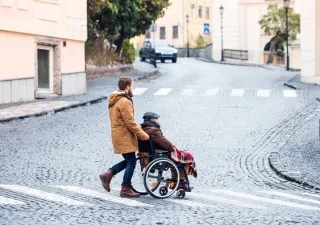 Una persona joven paseando a una persona mayor en silla de ruedas