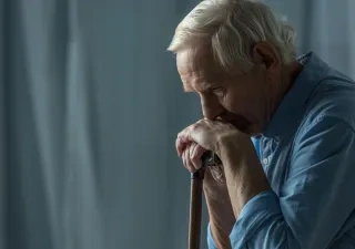 Persona mayor sentada en el sofa con la barbilla encima de su bastón