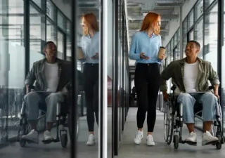 Chico con silla de ruedas hablando por la oficina con una compañera sin aparente discapacidad