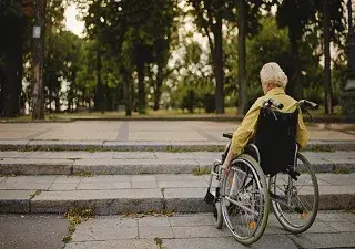 Una persona con movilidad reducida (PMR) y en silla de ruedas ante una escalera (Fuente: Rehatrans)