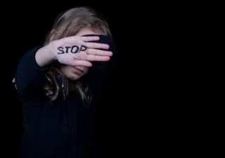 Una mujer pide el fin de la violencia de género con la palabra "stop" pintada en la mano mientras se tapa la cara con ella